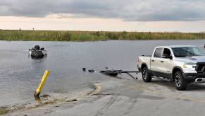 An image shows a RAM pickup truck backing up to the water to launch a boat.