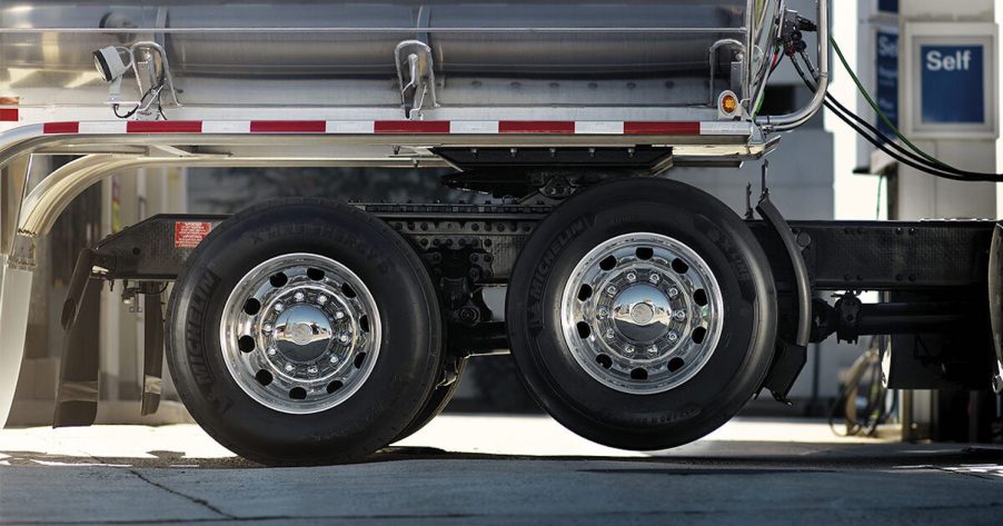 Lifted semi truck tag axle hanging beneath a trailer, the pavement visible in the foreground
