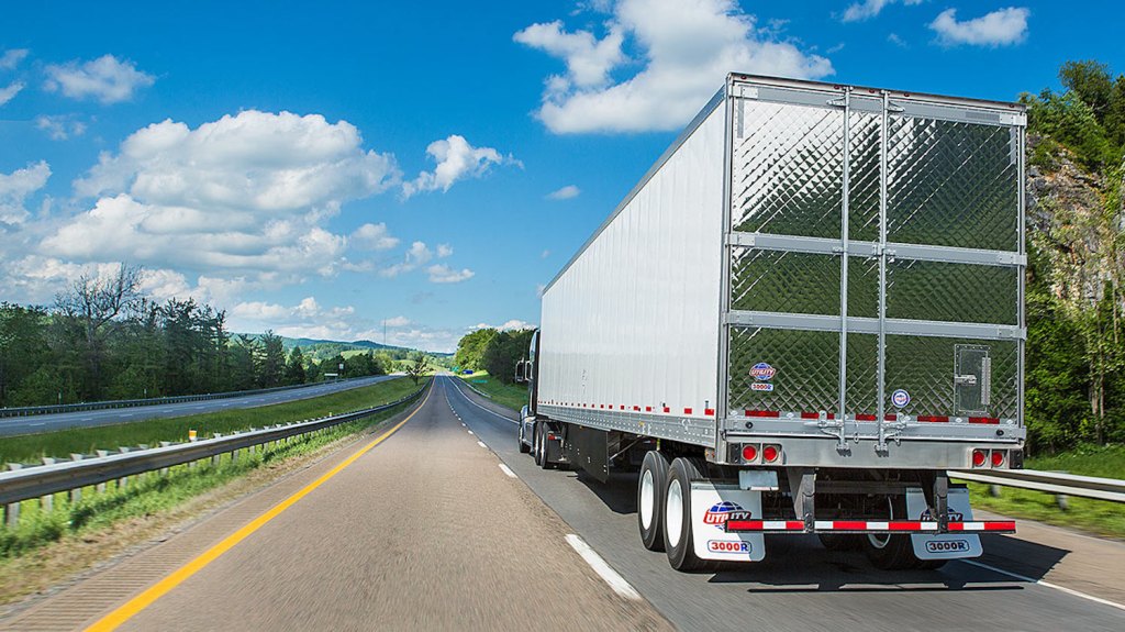 Semi truck driving down a highway, its trailer door finished in a shiny, quilted pattern