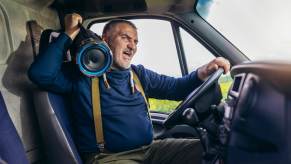 Italian man drives down the road singing with a boombox on his shoulder.