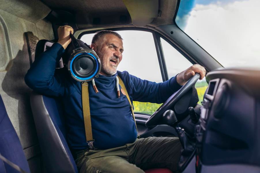 Italian man drives down the road singing with a boombox on his shoulder.