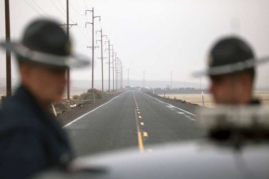 Two Oregon State police officers stand by a cruiser while stopping traffic on the highway.