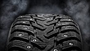 Closeup of winter tires with metal studs over a black background.