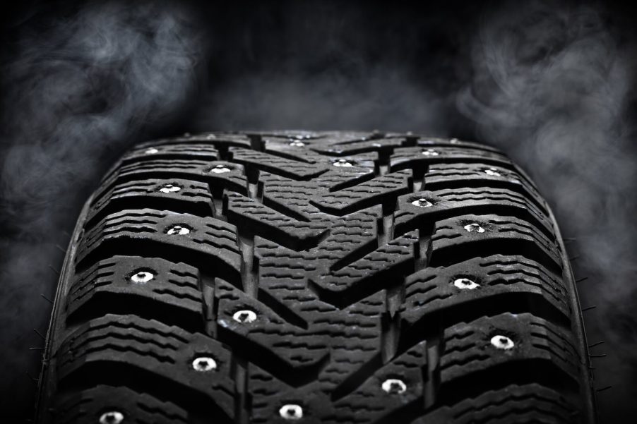 Closeup of winter tires with metal studs over a black background.