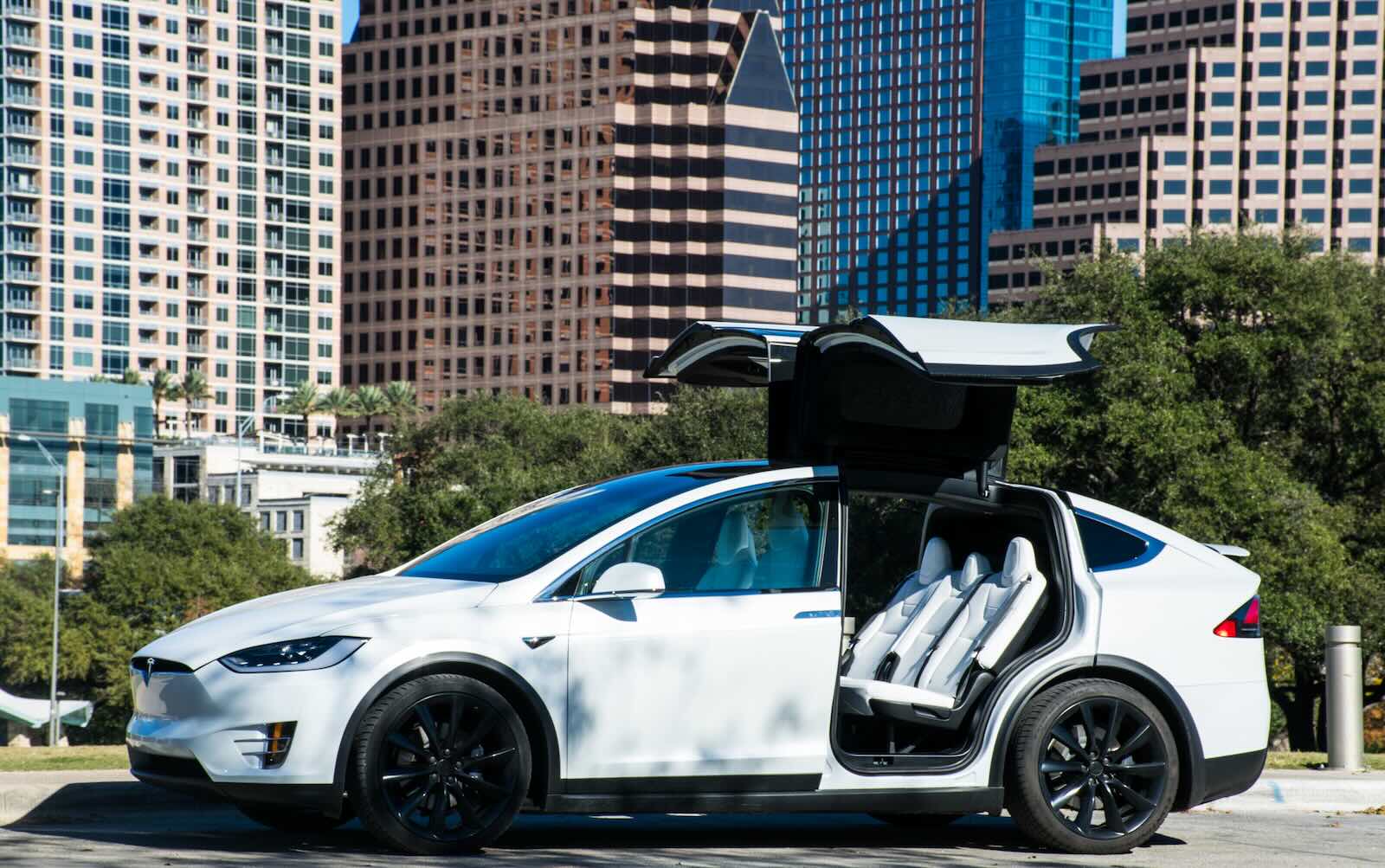 White Tesla Model X with gull wing doors open in front of NYC skyline.