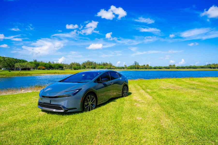Hybrid Toyota Prius car parked in a field, a river visible in the background.