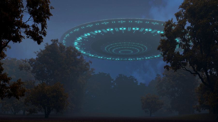 A depiction of a circular alien spaceship hovering close to a treelined night sky