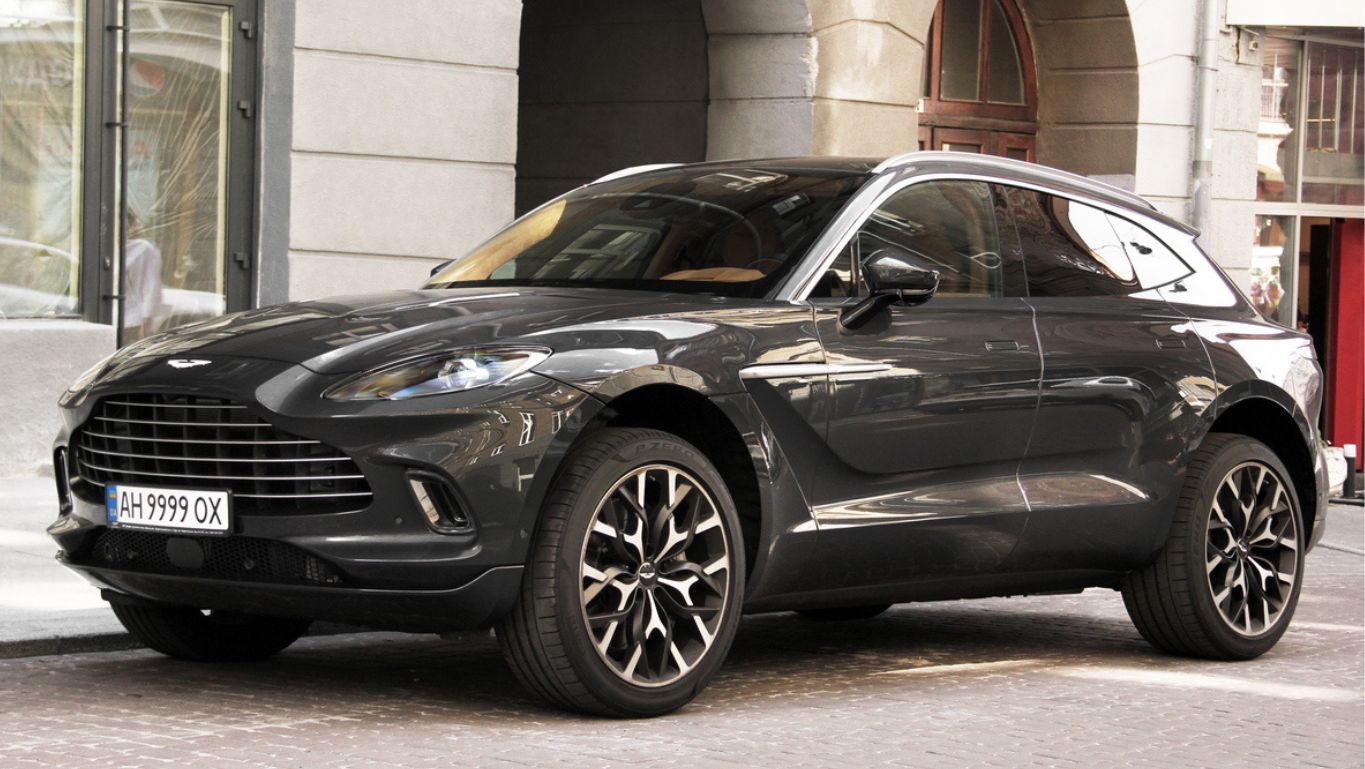 A dark-colored Aston Martin DBX parked on a city street in left front angle view