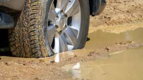 A close view of a car tire sunk down into a muddy road
