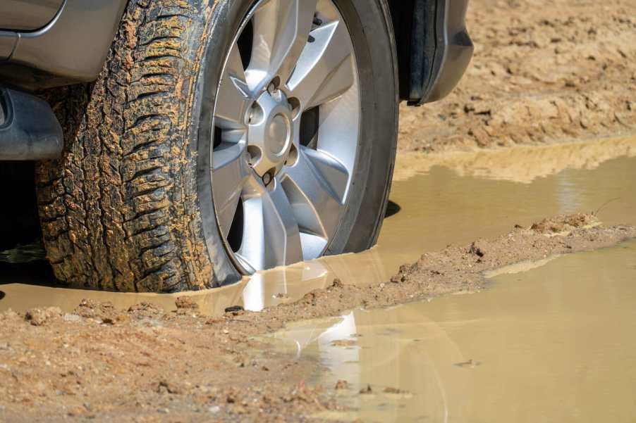 A close view of a car tire sunk down into a muddy road