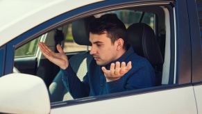 A confused male driver holding his hands up looking at car dash