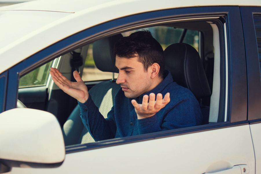 A confused male driver holding his hands up looking at car dash