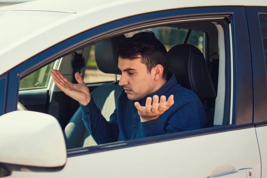A confused male driver holding his hands up looking at car dash