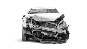 A light colored car shown in direct front view on white background after a head-on collision