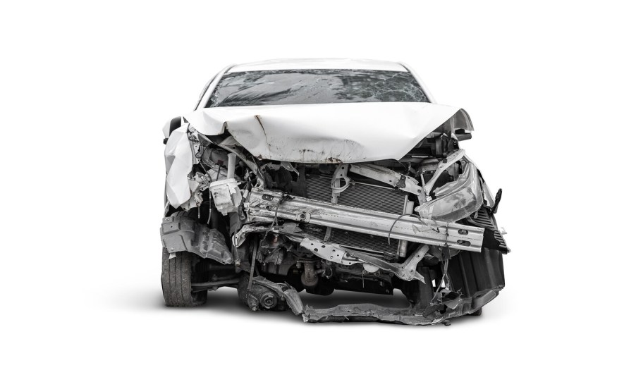 A light colored car shown in direct front view on white background after a head-on collision