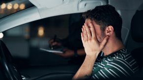 A driver covers their face with a police officer standing at opposite window at night in a depiction of a DUI investigation