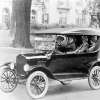 black-and-white photo of four people in a Ford Model T in a residential setting