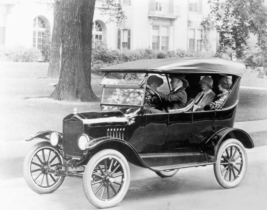 black-and-white photo of four people in a Ford Model T in a residential setting