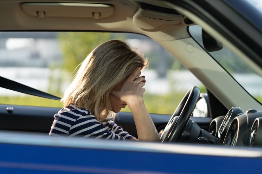 A blonde-haired female driver covering her face in frustration