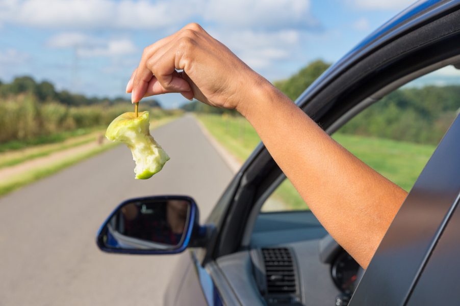 A woman's arm and hand holding an eaten apple out of the driver's side car window