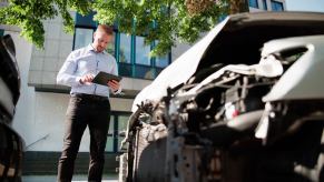 An insurance adjuster stands next to damaged car with a tablet