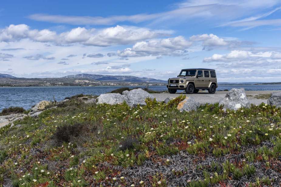 A gold Mercedes-Benz G-Glass parked on a rocky, grassy coast in far left front angle view