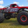 A red monster truck parked on grass in right profile view