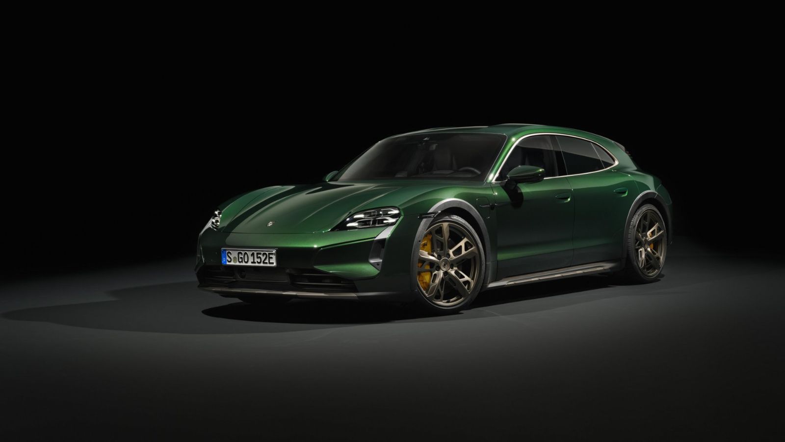 A green Porsche Taycan parked in a dark environment in left front angle view
