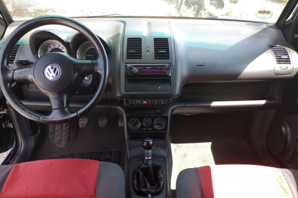 The black and red interior, dashboard, and transmission shift lever in a Volkswagen Lupo compact hatchback.
