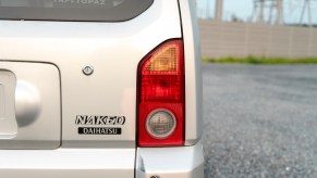 The "Naked" badge on the rear hatch of a Daihatsu Kei-car, a gravel lot visible in the background