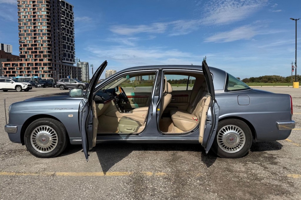 The rear-hinged rear doors of a luxury car parked in a lot, a high rise in the background.