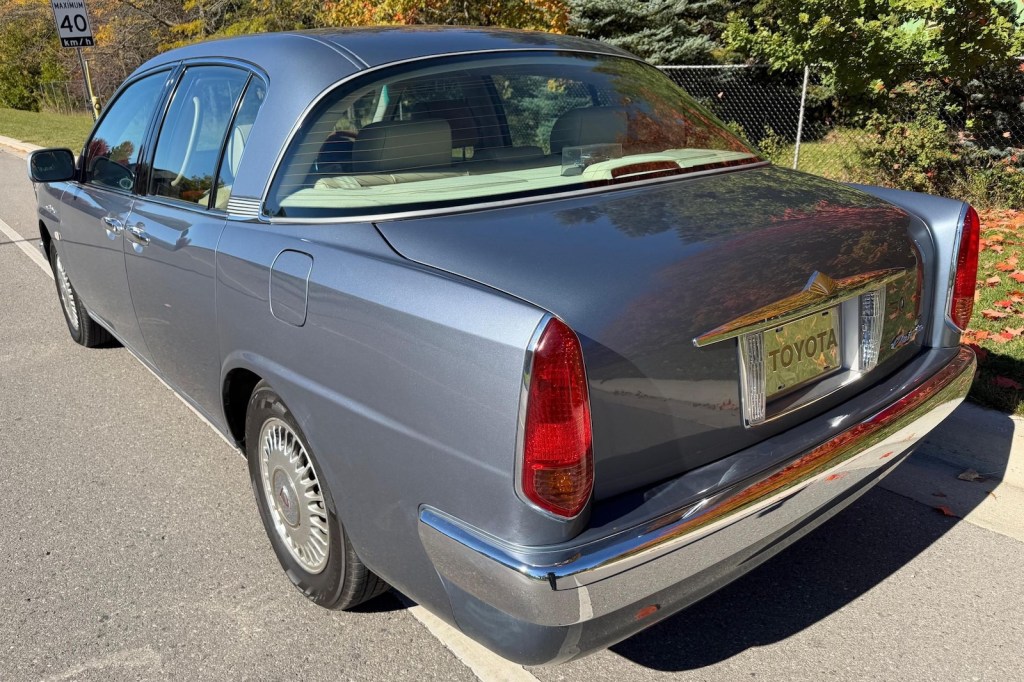 Wraparound rear glass and rear-angled C-Pillar of a handbuilt Toyota luxury car, trees visible in the background