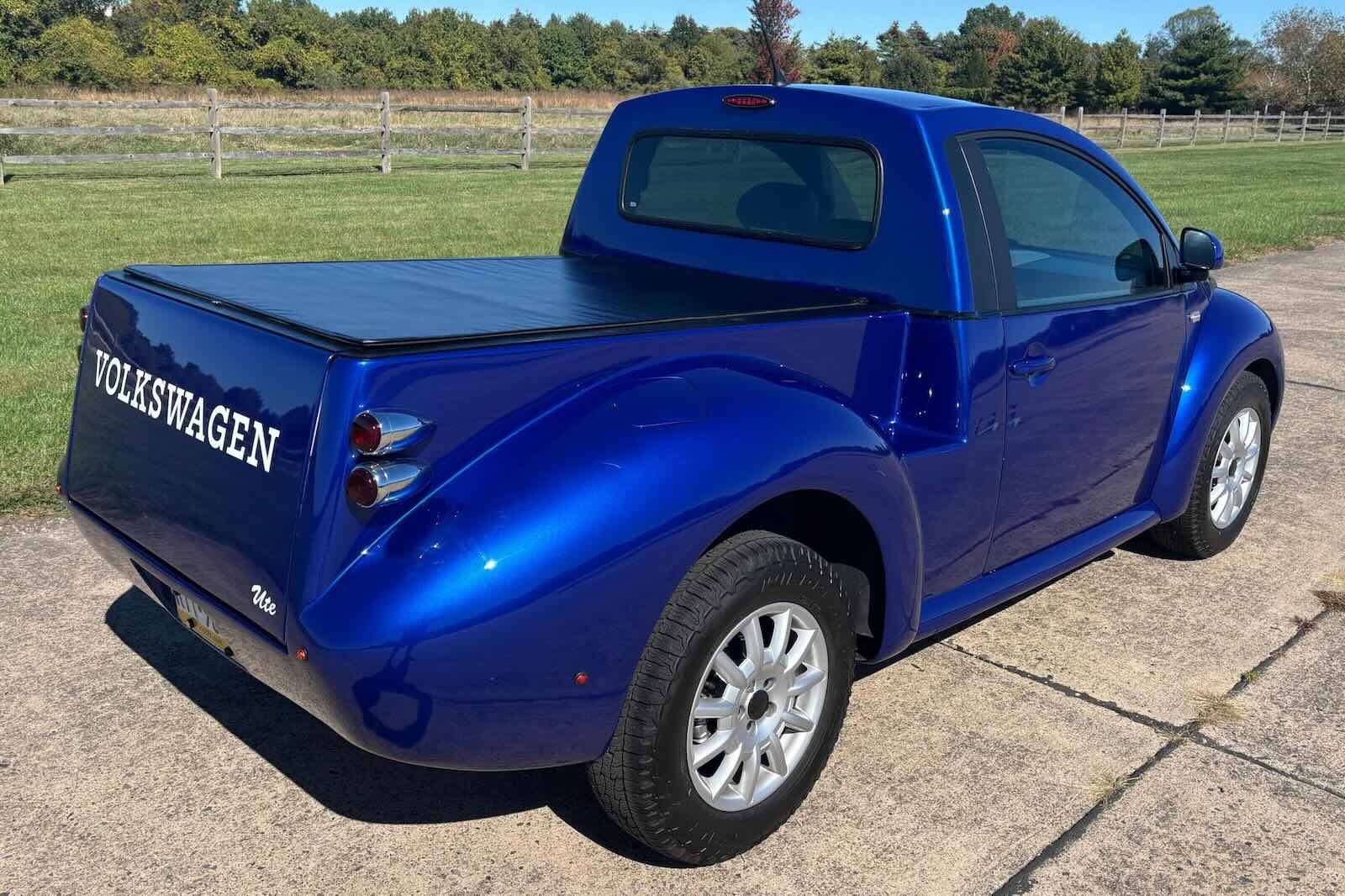 The bed of a blue VW New Beetle with a uterus conversion kit, parked in front of a farm