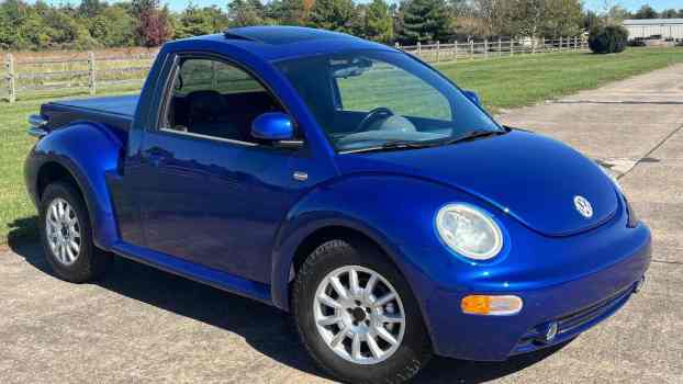The Volkswagen Beetle front end of a tiny pickup truck "ute" conversion, parked in front of a farm.