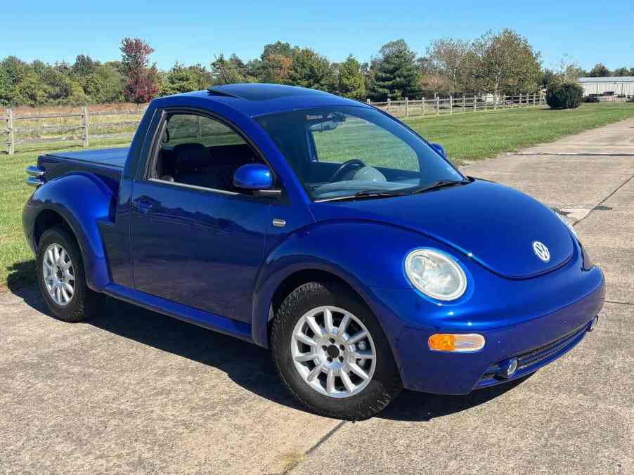 The Volkswagen Beetle front end of a tiny pickup truck "ute" conversion, parked in front of a farm.