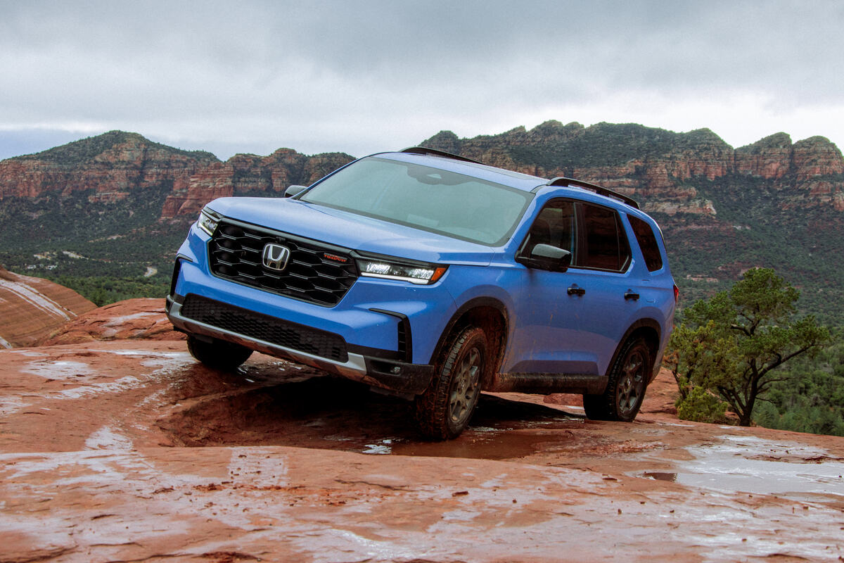A blue 2023 Honda Pilot TrailSport climbing a rocky ledge in left front angle view