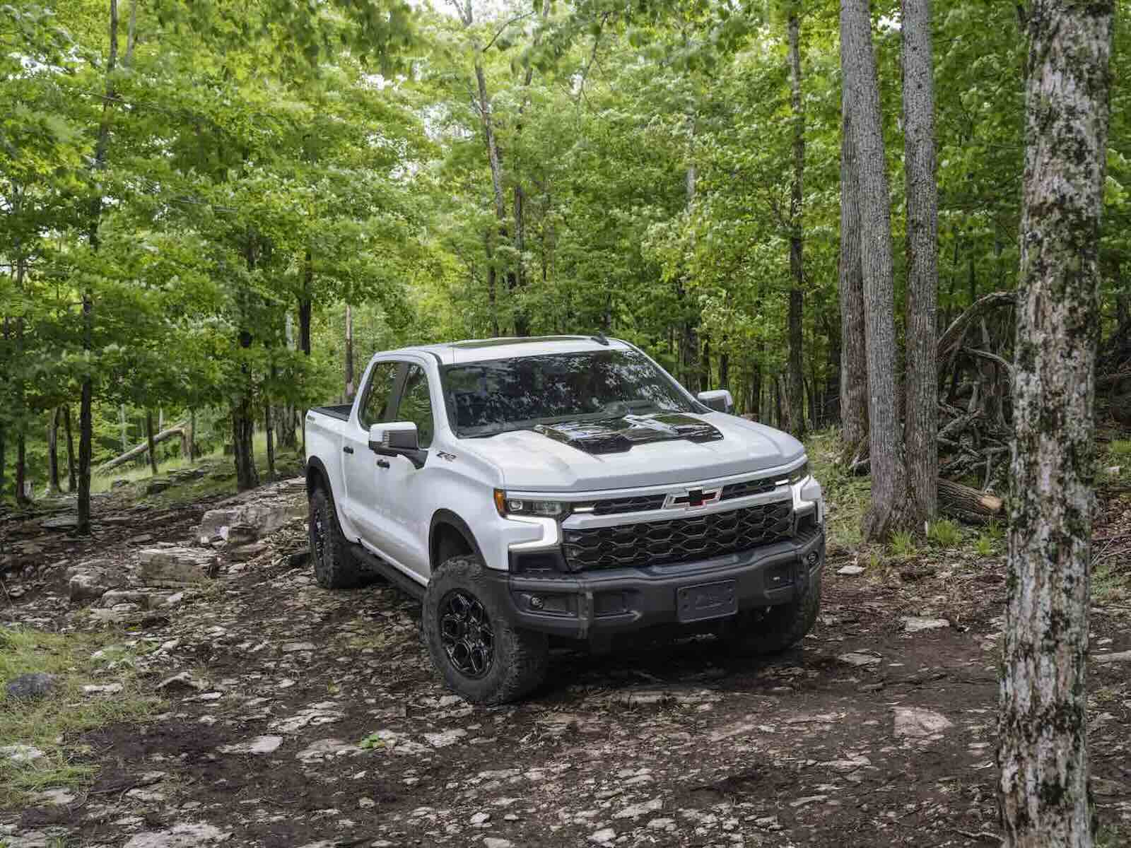 White Chevrolet Silverado pickup truck parked on rocks in the woods.