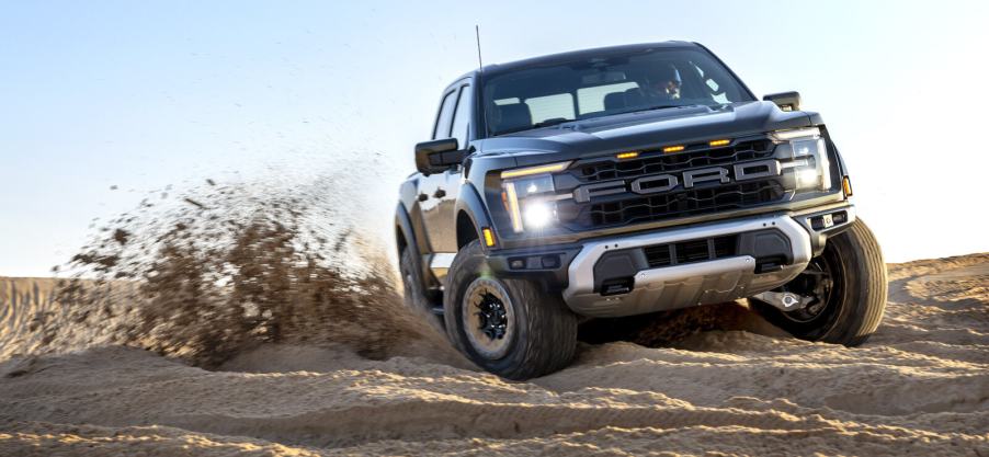 A dark-colored 2024 Ford F-150 Raptor drifting on off-road sand in front view