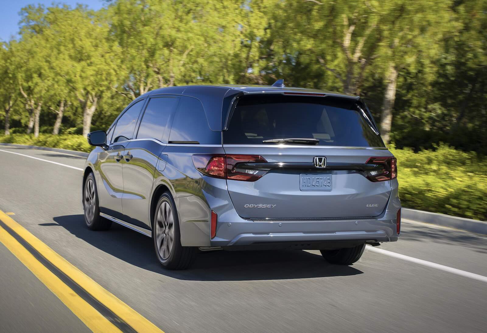 Honda's Odyssey minivan driving away on a  rural road, trees visible in the background.