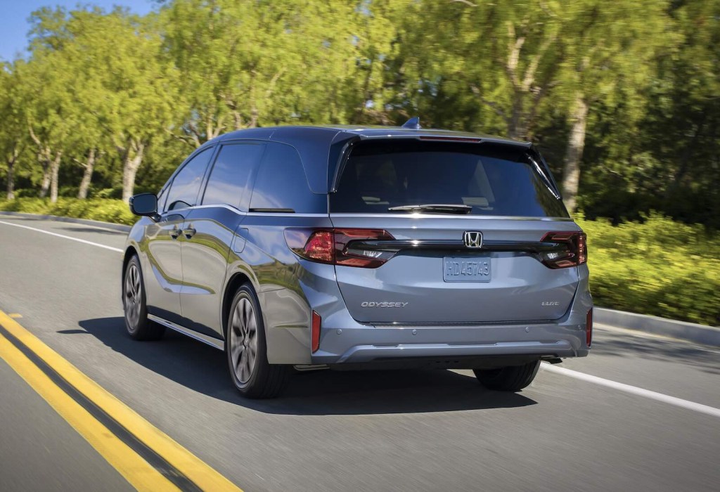 Honda's Odyssey minivan driving away on a rural road, trees visible in the background.