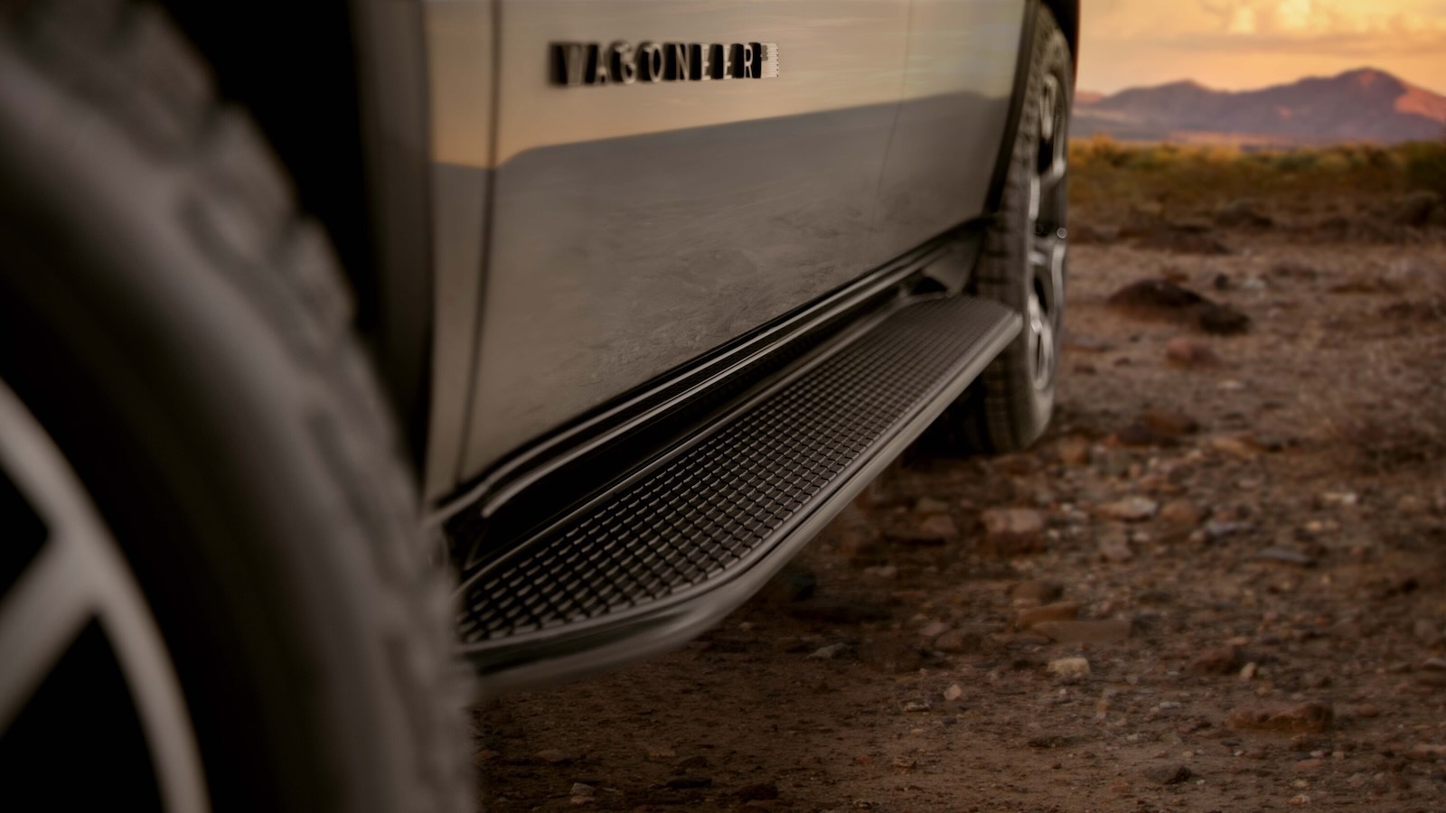 The Wagoneer badge on the side of a full-size Jeep SUV, mountains visible in the background.