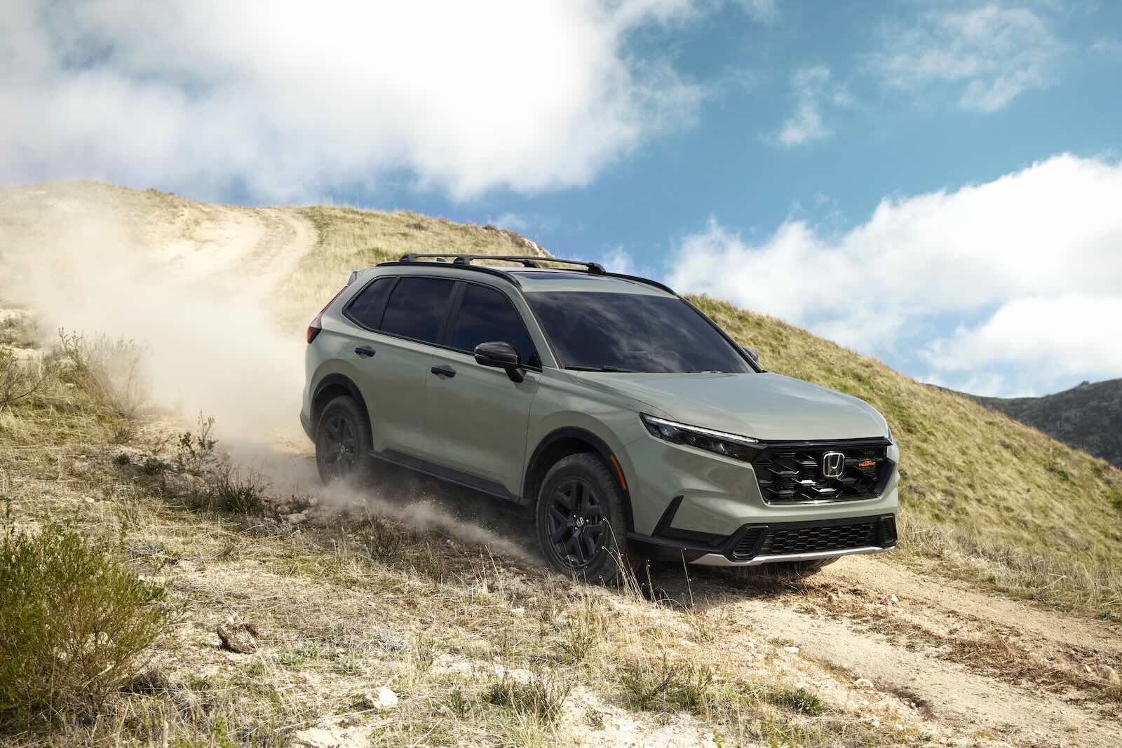 Honda CR-V crossover descends a dirt road, a mountain ridge visible in the background.