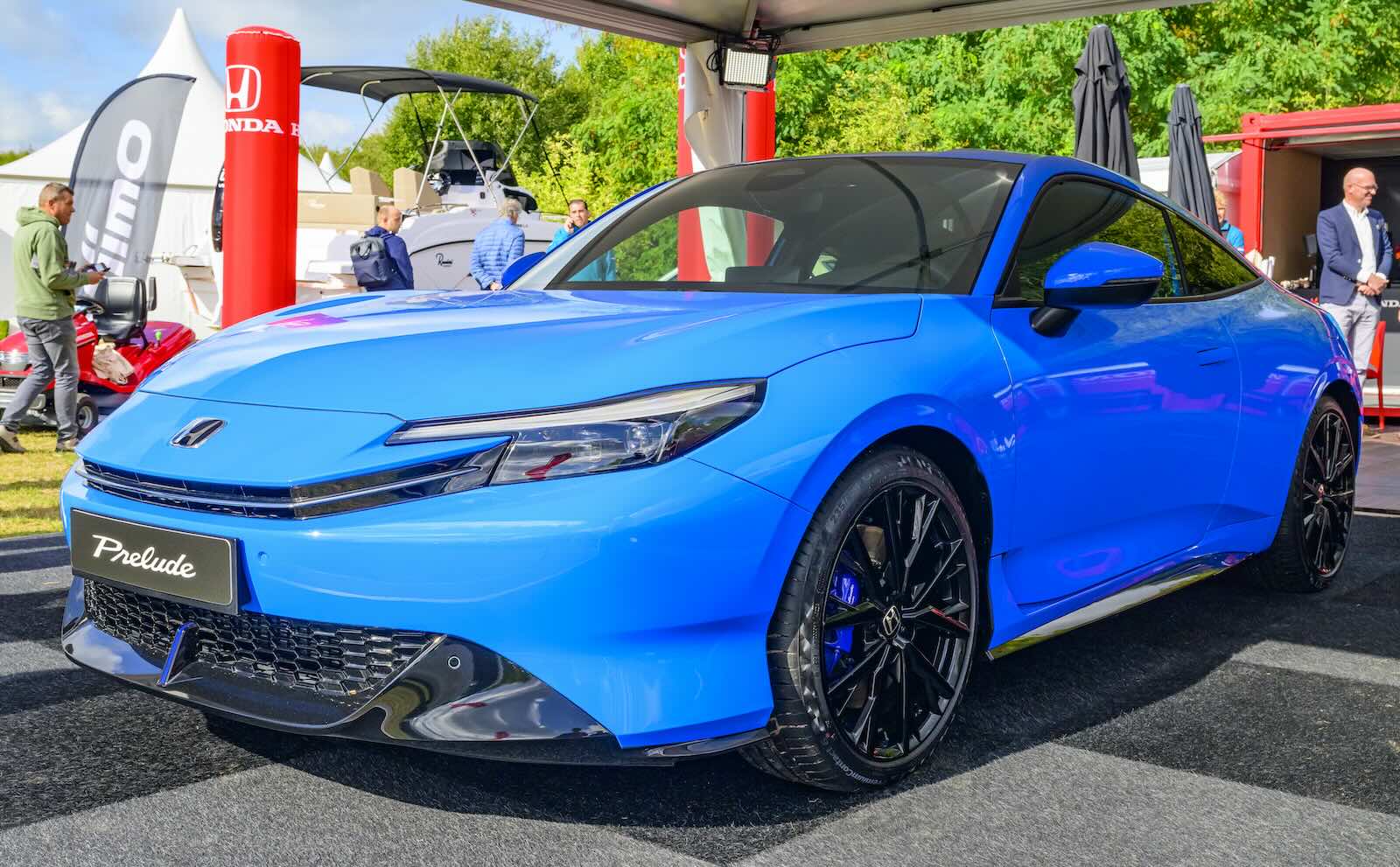 Bright blue Honda coupe sitting under a tent at an outdoor car show.