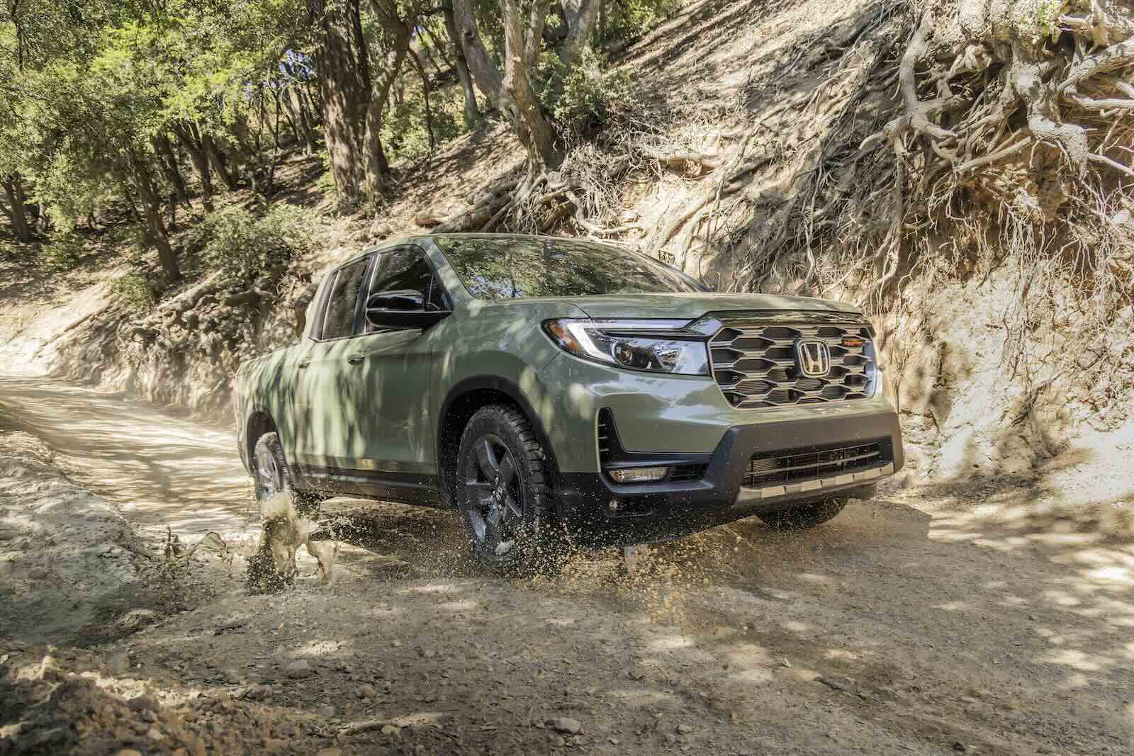 Ridgeline pickup truck driving up a muddy trail, trees visible in the background.