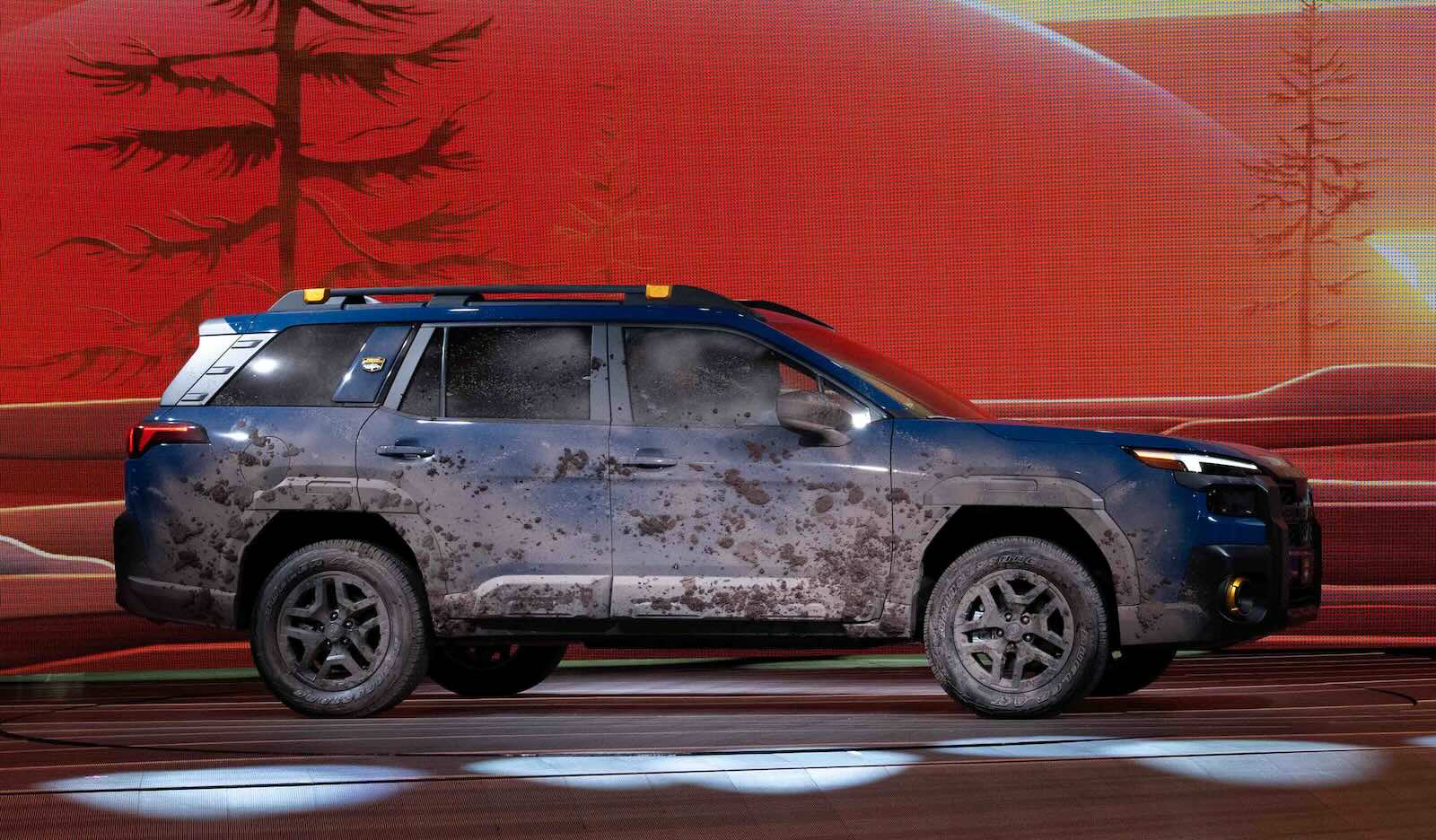 Redesigned Subaru Outback on stage at a car show, tree graphics in the background.