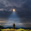 Man stands on the mountain top, studying glowing lights overhead.