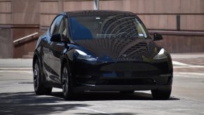 Black Tesla Model Y EV in a parking lot, a building visible in the background.