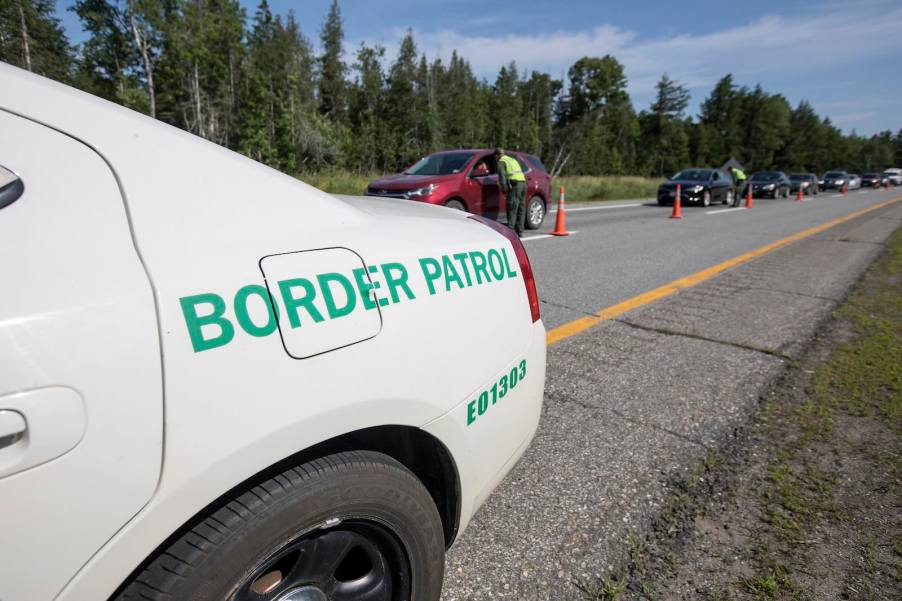The Border Patrol badging on the side of a white Dodge Charger patrol car parked on a rural road.