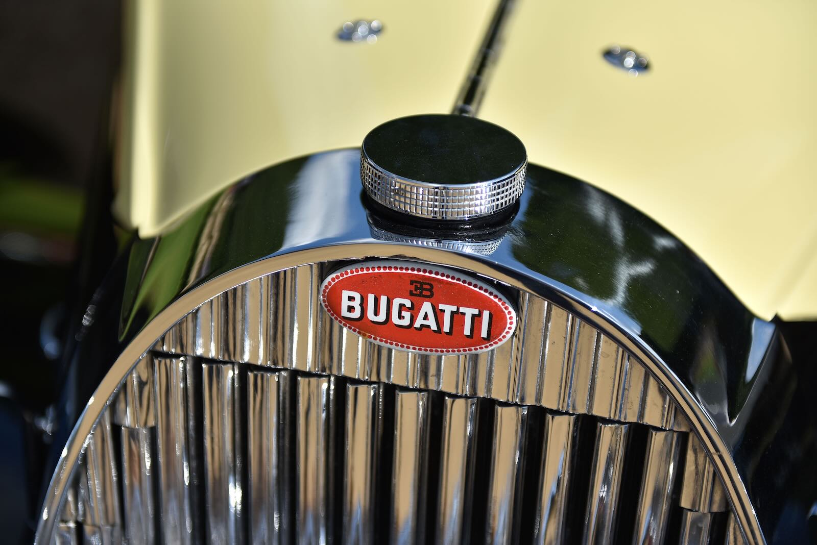 Red Bugatti badge on the  horseshoe grille of a yellow Atalante classic car.
