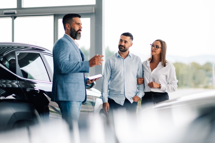 Car salesman standing in a dealership and showing customer the redesigned makes and models for 2026